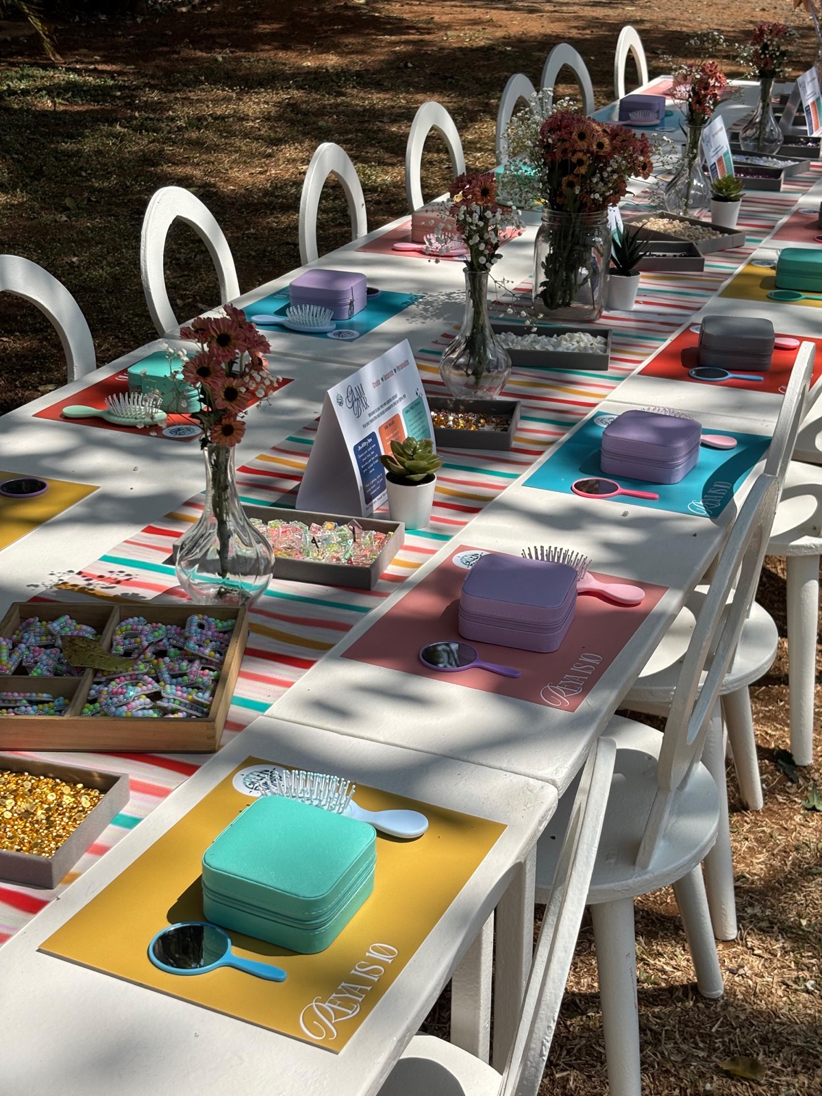 A long outdoor table set with a decorating place for each child — brushes, jewellery boxes, mirrors and flowers down the centre