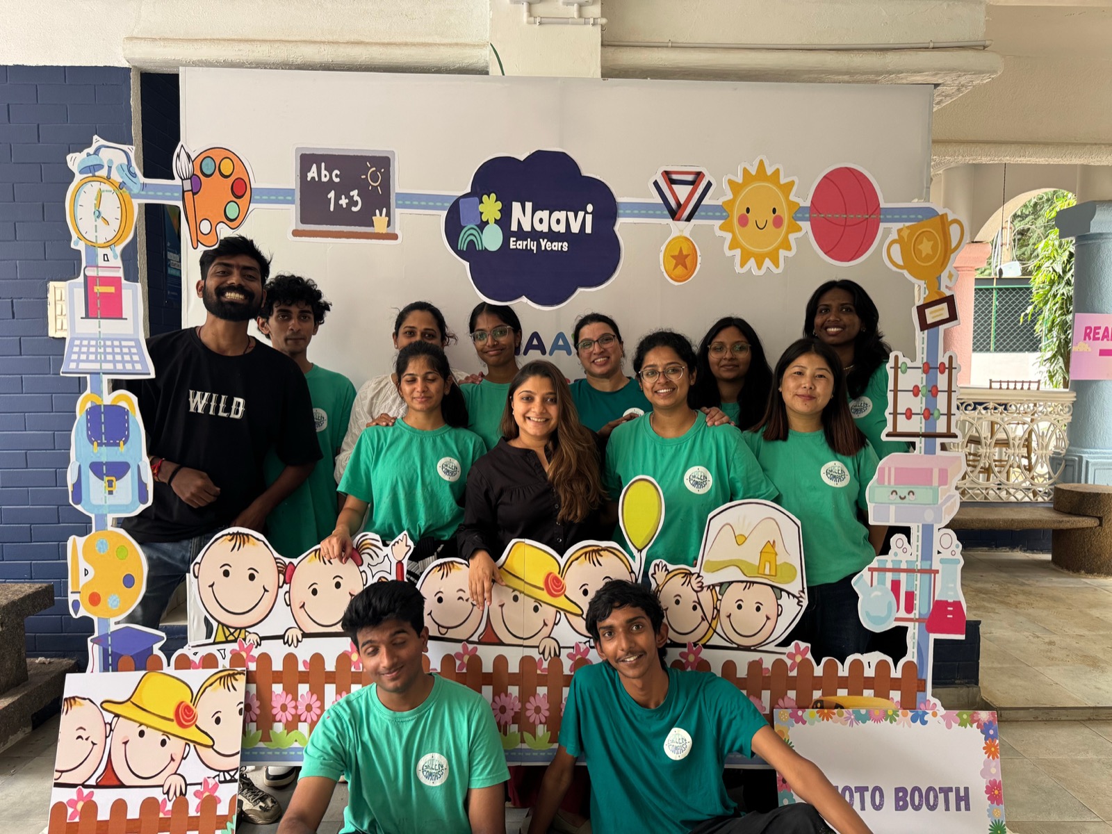 The Green Compass team in their green shirts, gathered around a photo booth frame at a school event